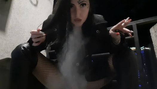 Heiße und sexy Domina Nika raucht eine Zigarette auf ihrem Balkon und bläst Rauch in dein Gesicht.