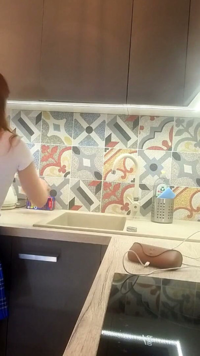 Chica universitaria real, petite y caliente, con uniforme escolar de cuadros y minifalda, enseña sus piernas y bragas de algodón en la cocina | Clip 1