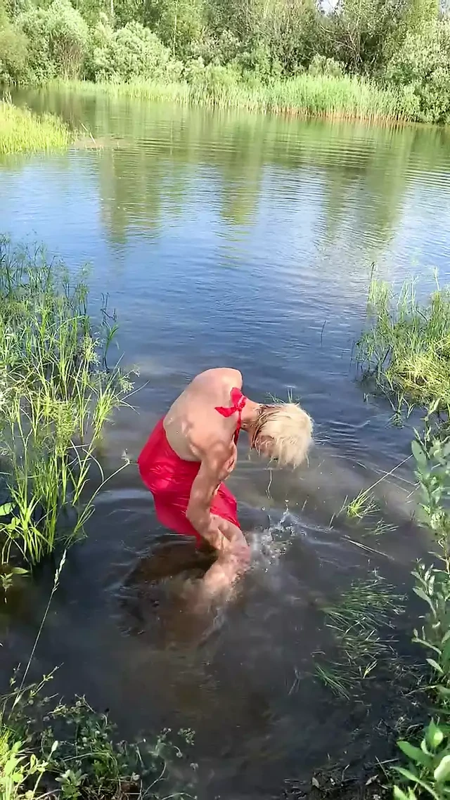 Swimming in lake in coral color summer dress and white sneakers. Wet dress. Wetlook transgirl