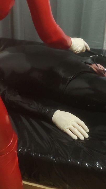 Hot MILF in a Red Latex Catsuit She Is Enjoying It with a Locked Slave. Second Angle