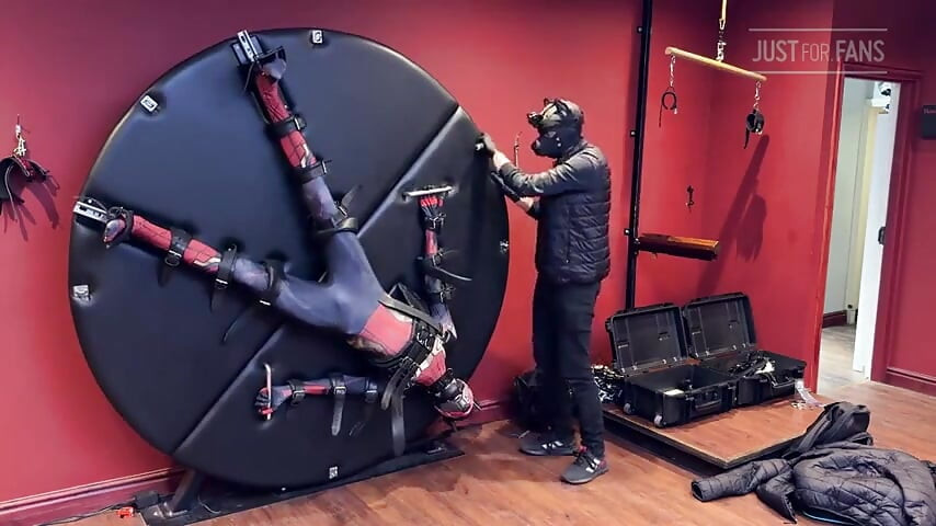 Filhote twink vestido de homem-aranha amarrado à roda de escravidão e ordenhado