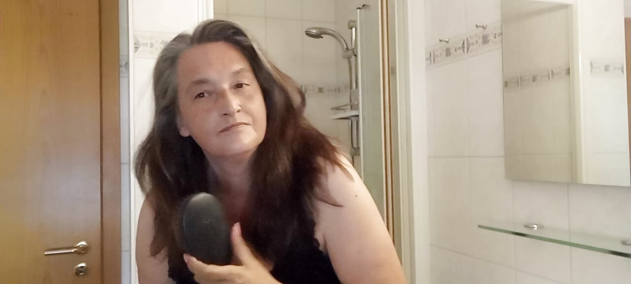 Зрелая женщина с настоящими серебряными прядями медленно расчёсывает свои длинные волосы