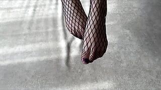Ein Mädchen in schwarzen Netzstrumpfhosen streichelt ihre Beine