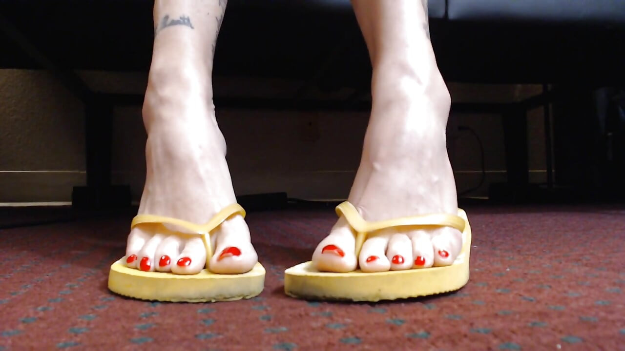 Červený nehet vratící se žluté flipflops