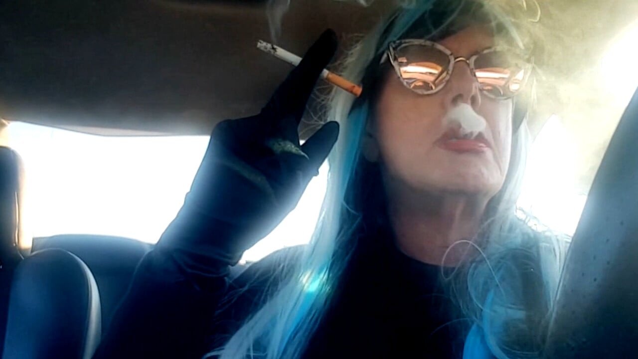 UN CD MATURE FUME ET CONDUIT AVEC UNE CIGARETTE MB100 DANS SA MAIN GANTÉE