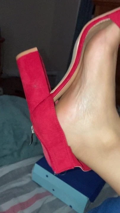 Dangling kasut tumit merah seksi di atas katil