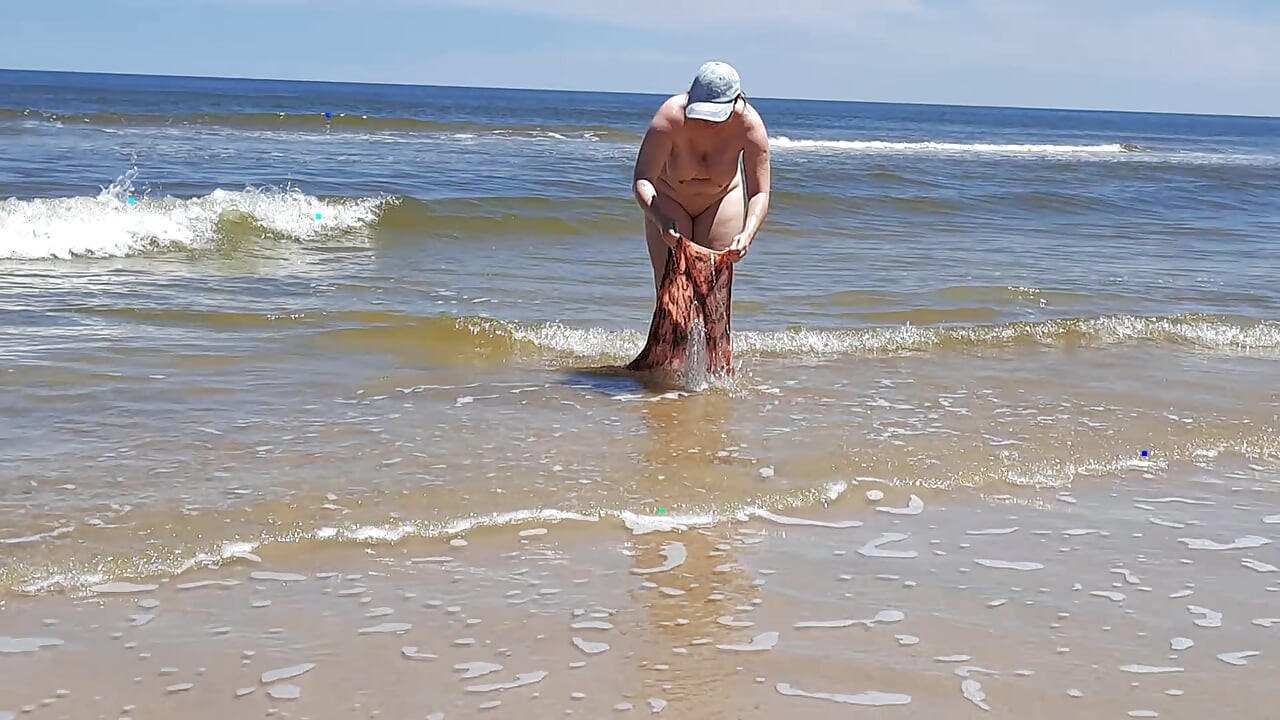 Filmare de amatori. Un nudist se joacă cu valurile pe malul oceanului.