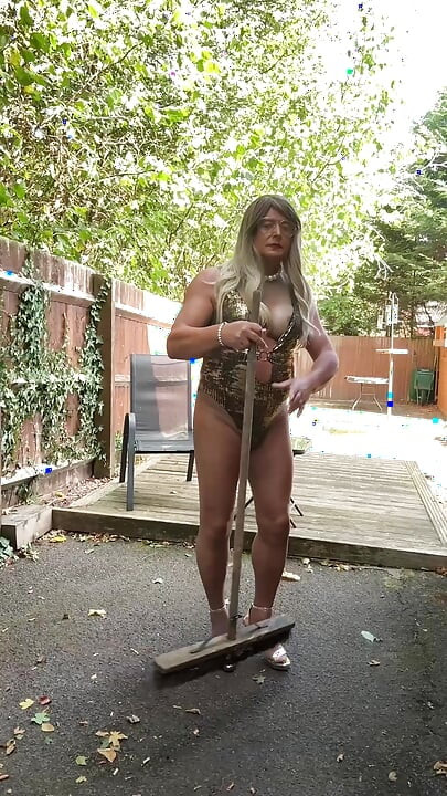 Seksi transvestit kellycd2022 u zlatnom kupaćem kostimu i štiklama čisti lišće