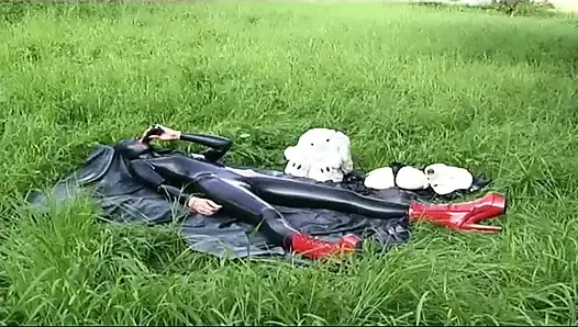 Fetisch-sklavin in latex geht und lutscht einen dildo auf dem gras