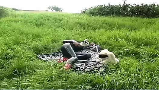 Fetisch-sklavin in latex geht und lutscht einen dildo auf dem gras