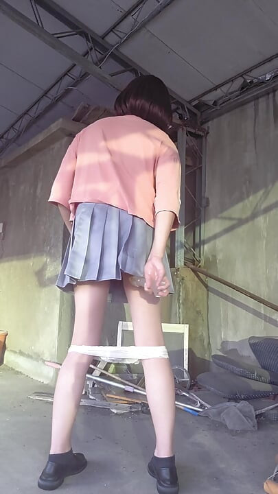 Beyaz iç çamaşırıyla eşleşen pleated bir etek ve terasa anal tıkaç takıyor