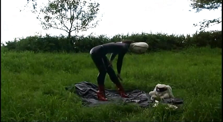 Fetish slave in latex walks and sucks a dildo on the grass
