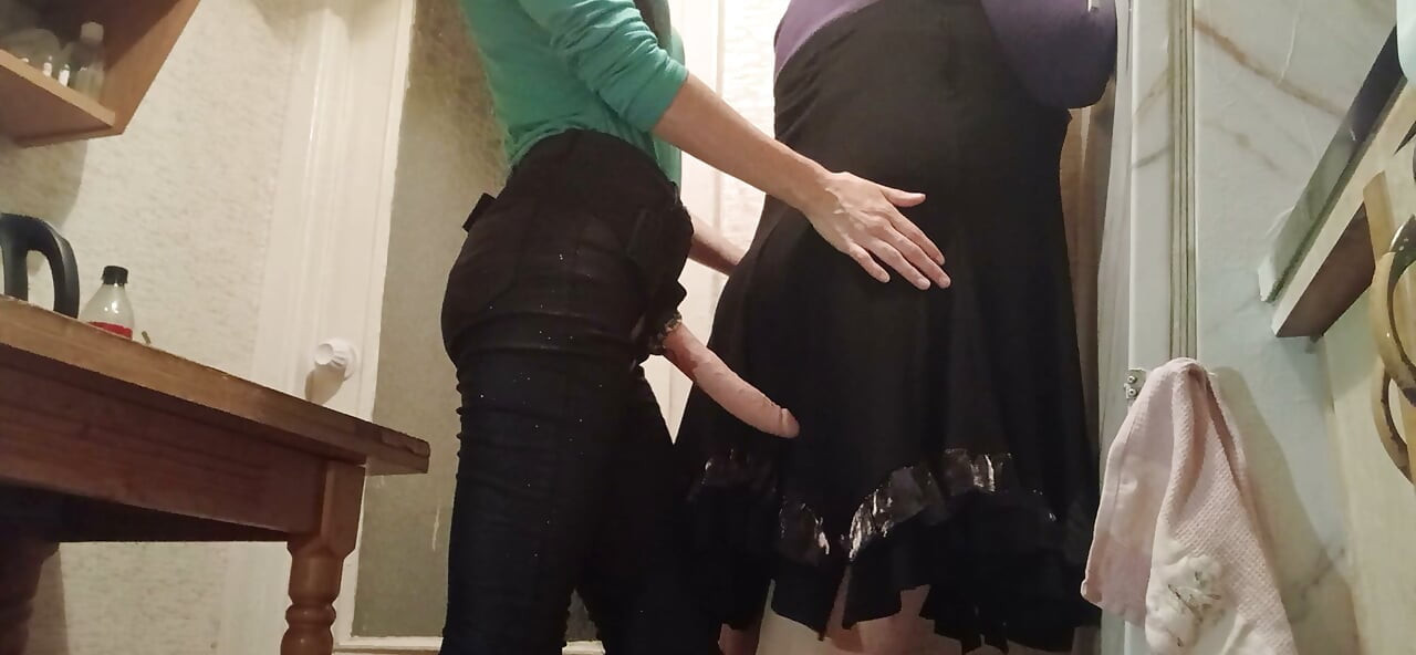 I’m fucking my married neighbor hard with a strap-on in the kitchen while her husband watches TV