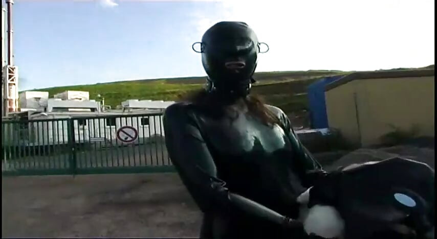Nô lệ tôn sùng trong latex đi bộ và bú một dương vật giả trên cỏ