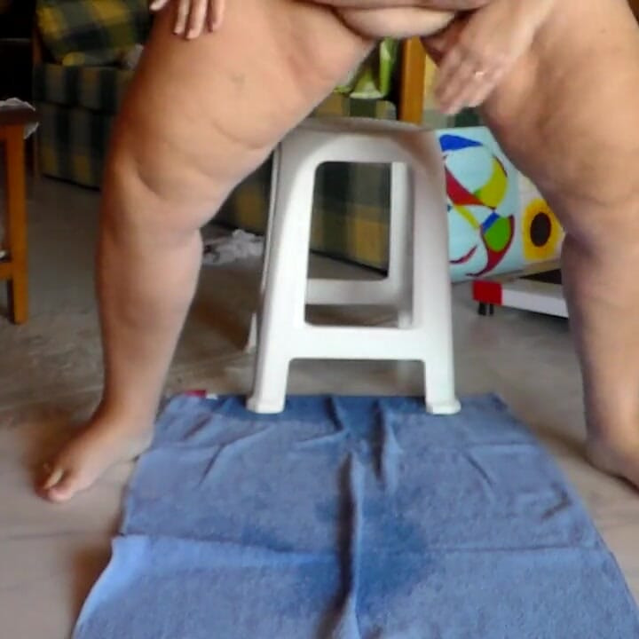 Jen está sentada em uma cadeira e fazendo xixi em uma toalha no chão