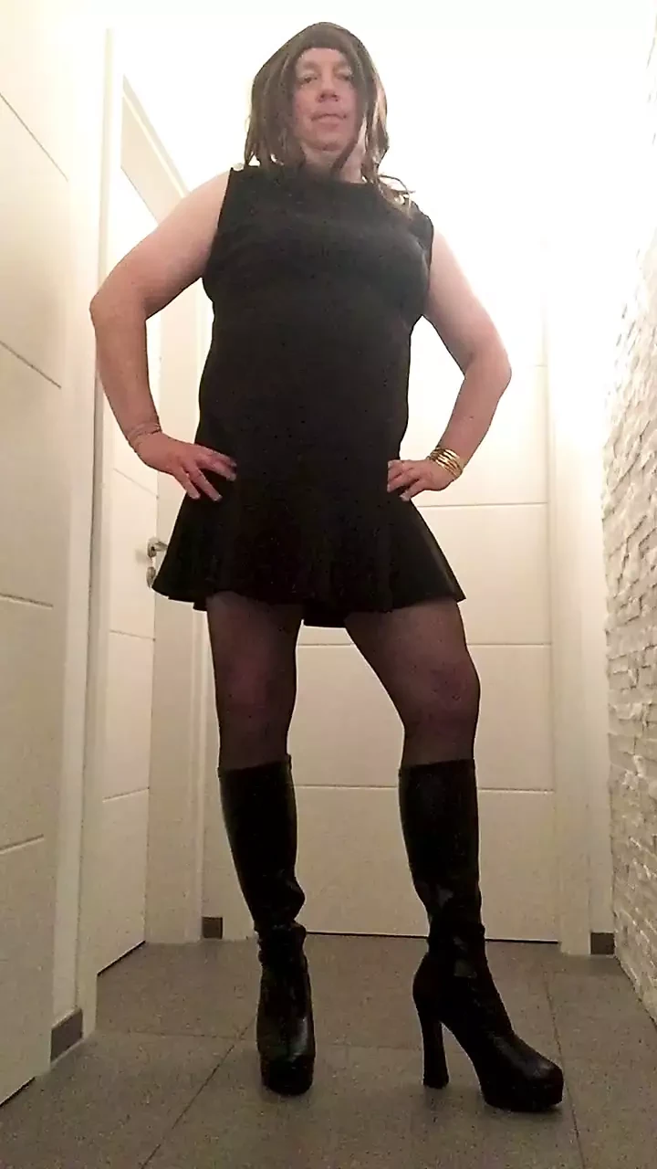 Nicki-travestito in un abito nero sexy, calze e stivali con il tacco alto