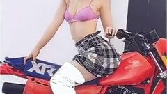 Dove Cameron in a pink bra straddling a motorcycle