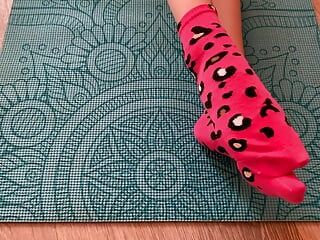 Gloria Gimson en chaussettes roses caresse ses pieds sur un tapis de yoga