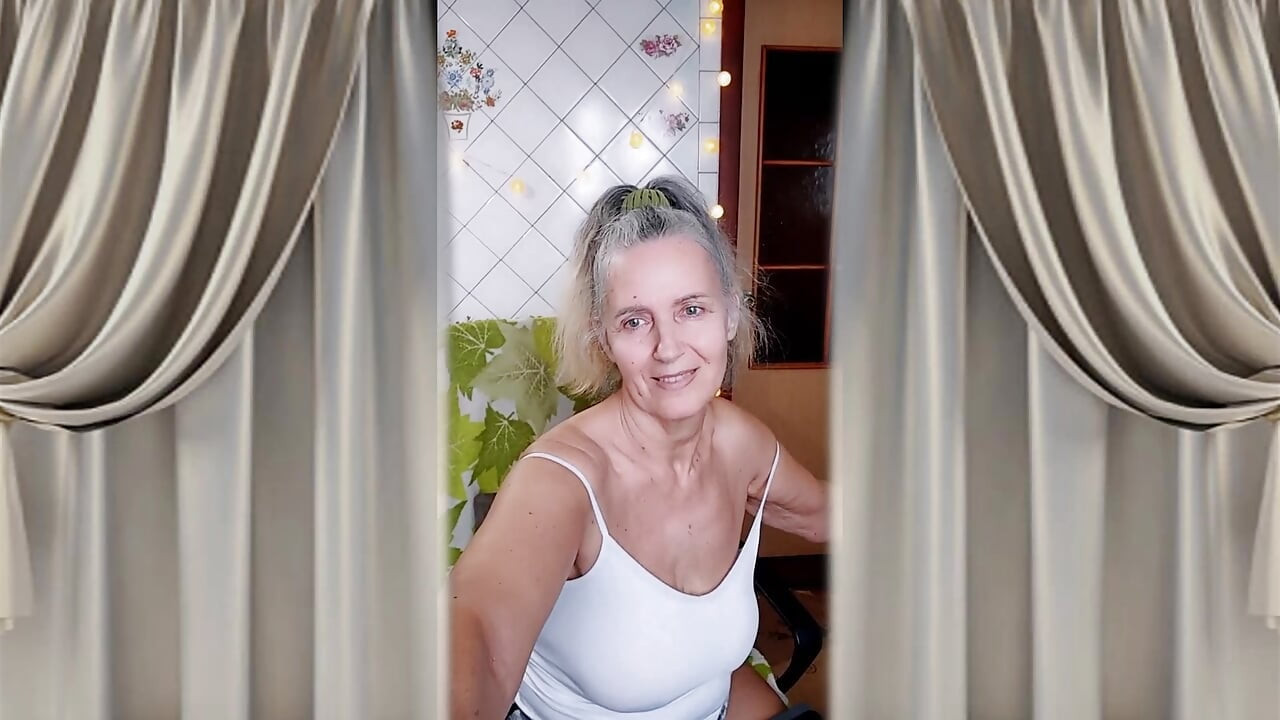 A cheerful housewife twerks in the kitchen near the washing machine and beckons with her bare feet.