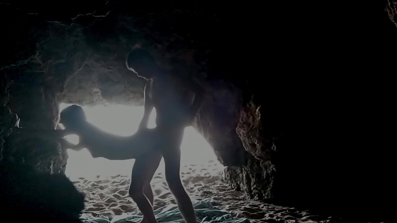 Casal gravado na praia, dentro da caverna