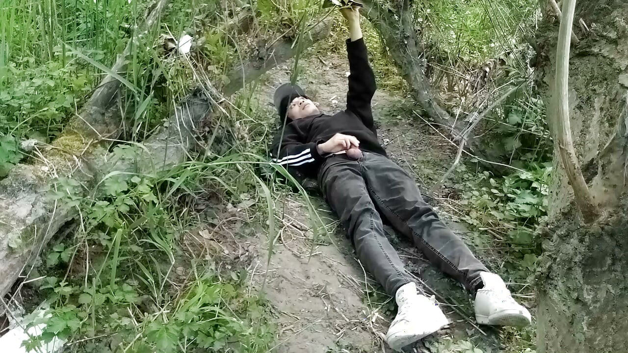 The cute gay twink jerking off his cock, pulled through his fly while outdoors, is Jon Arteen