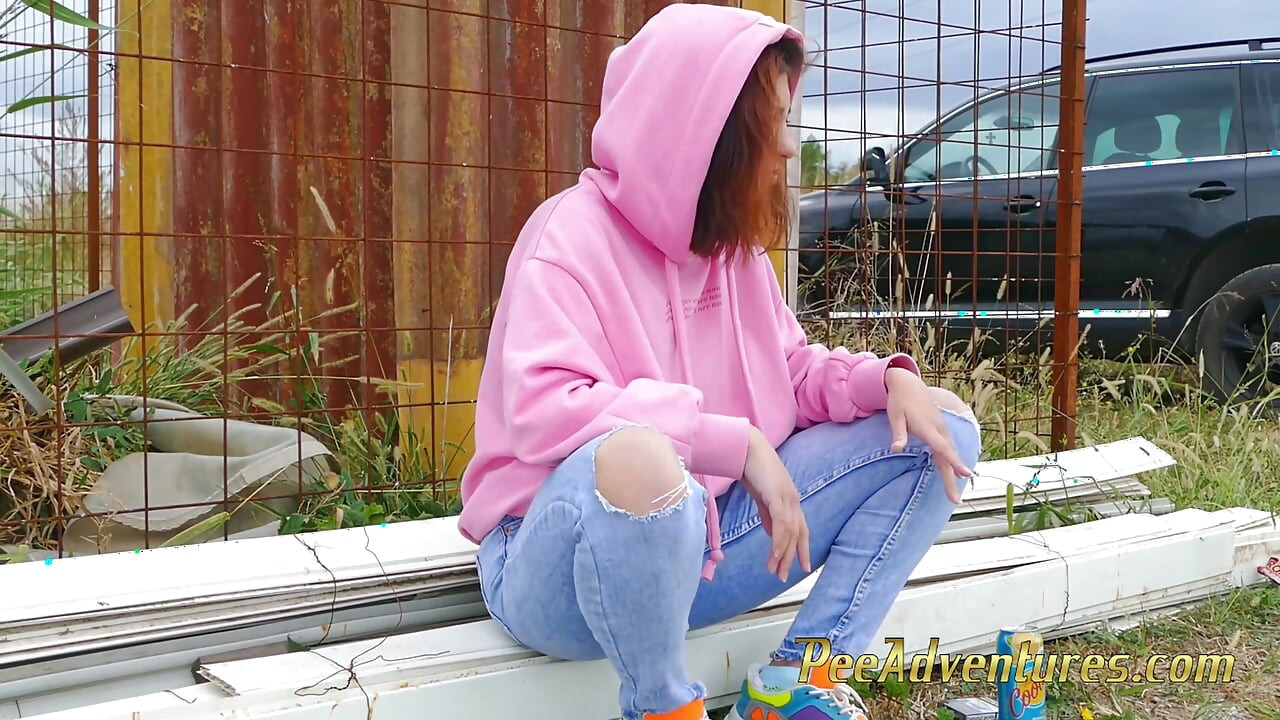 Hipster girl with a hoodie pee trough her jeans and pee next to the wheel of the car