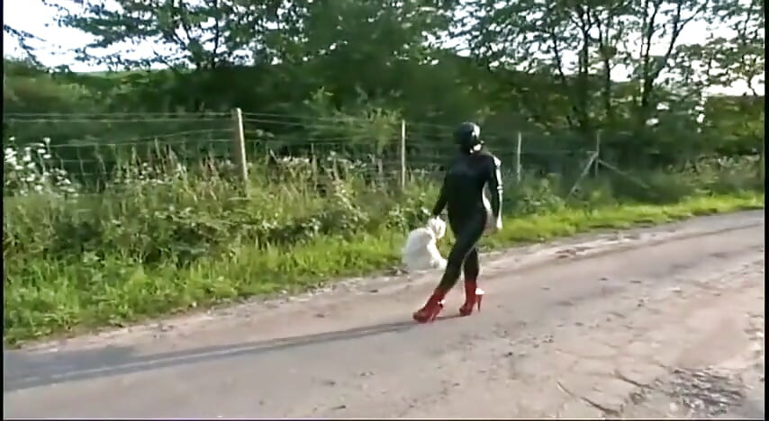 Fetish slave in latex walks and sucks a dildo on the grass