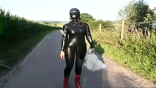 Fetish slave in latex walks and sucks a dildo on the grass