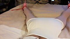 Laura trägt ein sexy weißes Kleid, rosa Strumpfhosen und Plateau-Absätze, ist gefesselt und wird in einem Bett geknebelt