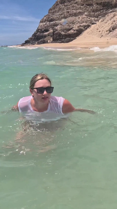 Menina molhando jeans no oceano e nadando em camiseta branca molhada