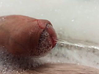 Gros plan sur une bite en train de pisser dans la mousse de la baignoire