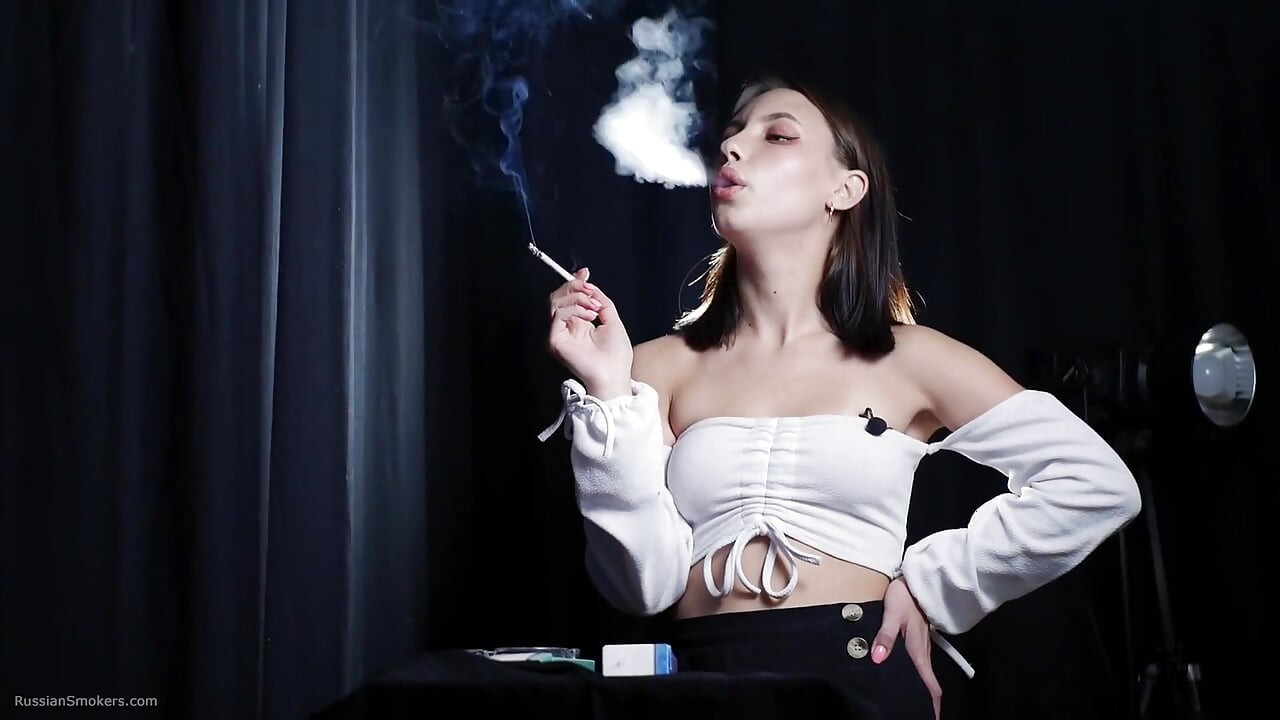 Elegante morena fumando cigarro em cena de estúdio escuro