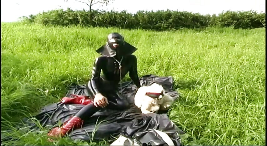 Fetish slave i latex går og sutter en dildo på græsset