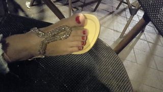 Freundin zeigt ihre sexy pedikürten Füße und Zehen in neuen Sandalen im Café