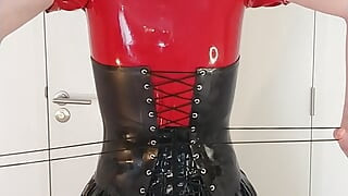 Putting on locked rubber corset and long latex skirt over red hooded dress and maid stockings, layers