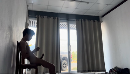 A handsome young man jerks off in front of a glass door.