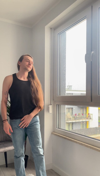 Long-haired boy masturbates in front of big window
