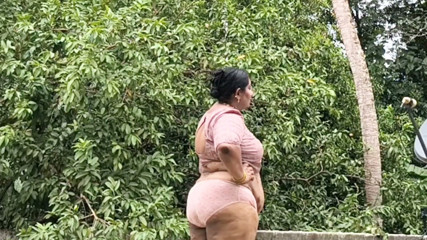 A full-figured woman in a white skirt and pink top strips down and walks nude outside.