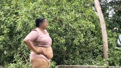 A full-figured woman in a white skirt and pink top strips down and walks nude outside.
