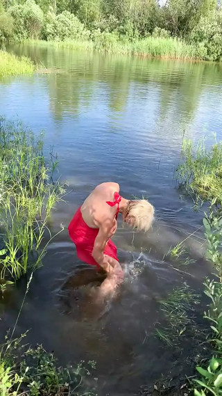 Swimming in lake in coral color summer dress and white sneakers. Wet dress. Wetlook transgirl