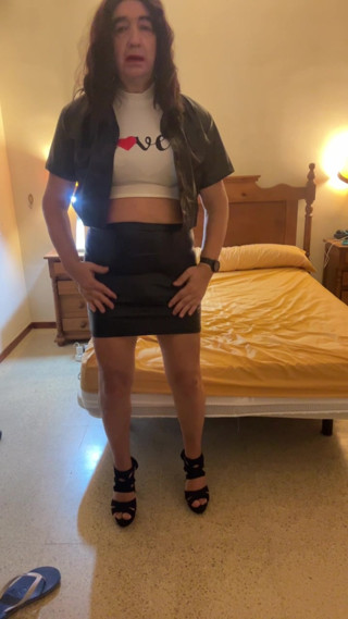 Beautiful and sexy Spanish trans girl masturbates in a tight miniskirt and black latex jacket in the bedroom, wearing high heels