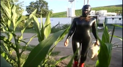 Fetish slave in latex walks and sucks a dildo on the grass